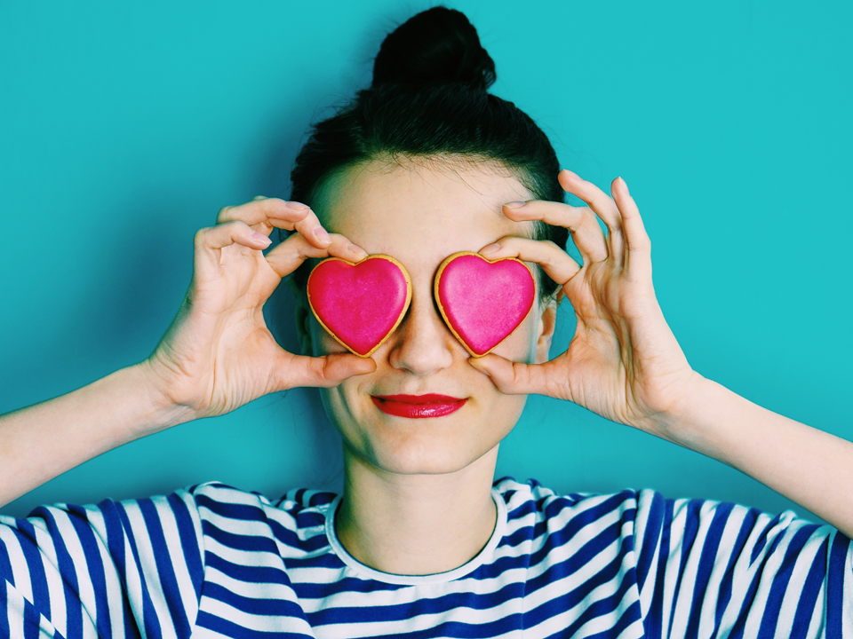 girl holding heart-shaped cookies against her eyes