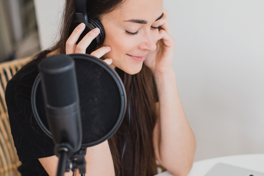 young woman recording online podcast using studio microphone and earphones